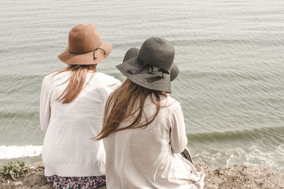 Women on the seashore sitting down on the sand, watching the sea together 