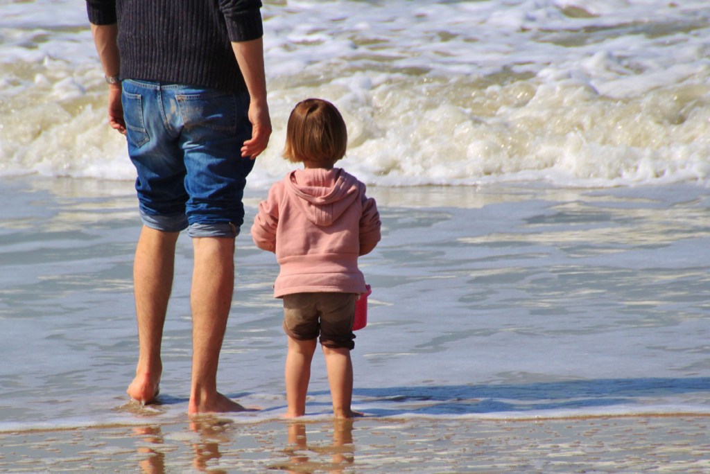Father and daughter on the beach, at the edge of the sea, with feet in water (Father's Day wishes)