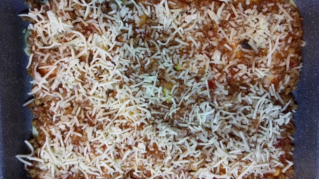 Adding half the shredded cheese on top of the zucchini slices and the meat mix