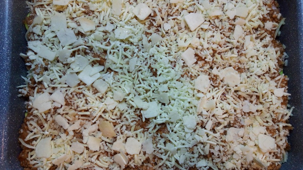 Adding the second half of the shredded cheese and the Parmesan flakes to the top of the zucchini lasagna