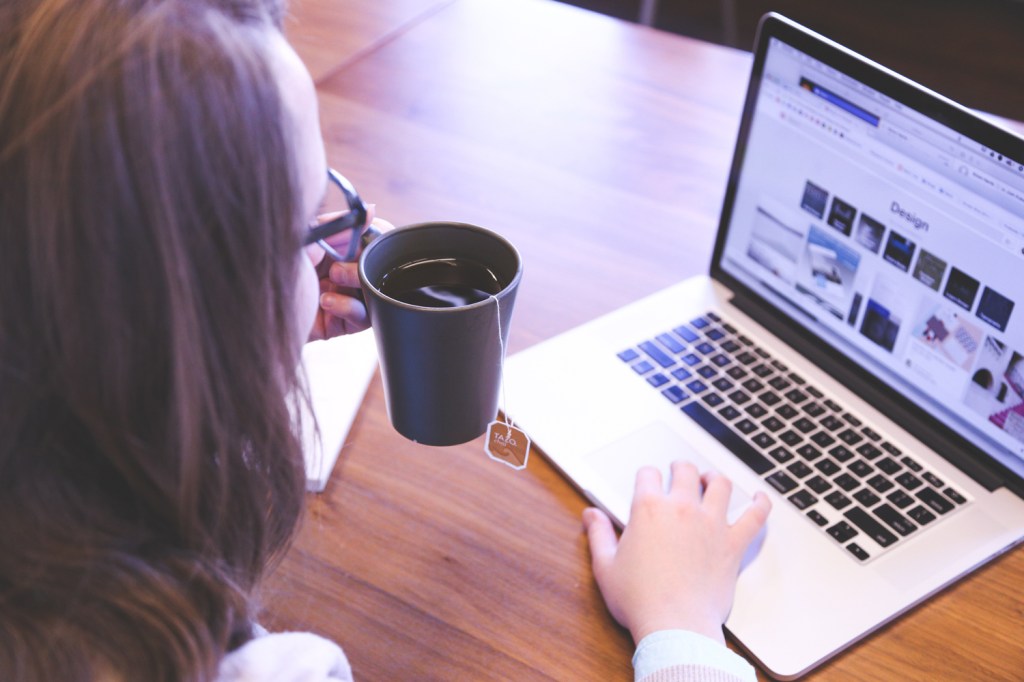 Young woman working at a laptop while holding a cup of coffee