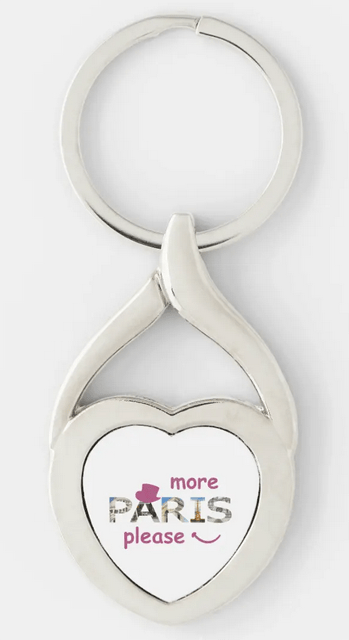 Cute heart-shaped keychain with "more Paris please," with top tourist attractions through the letters and a cabaret hat and a smile. With faux pink glitter